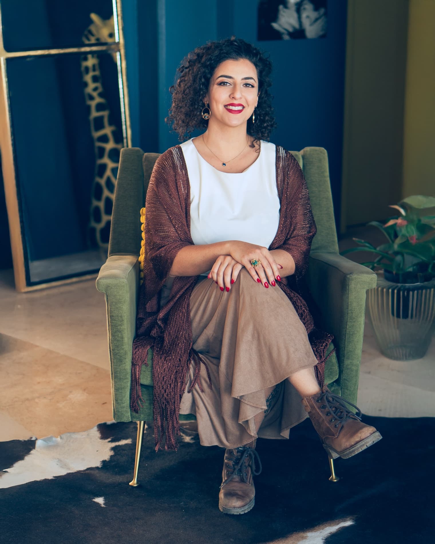Asha Singh, psychotherapist for psychedelic preparation and integration, seated in a green armchair and smiling at the camera.