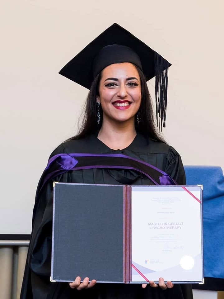 Asha Singh in graduation cap and gown, holding her Master in Gestalt Psychotherapy diploma.