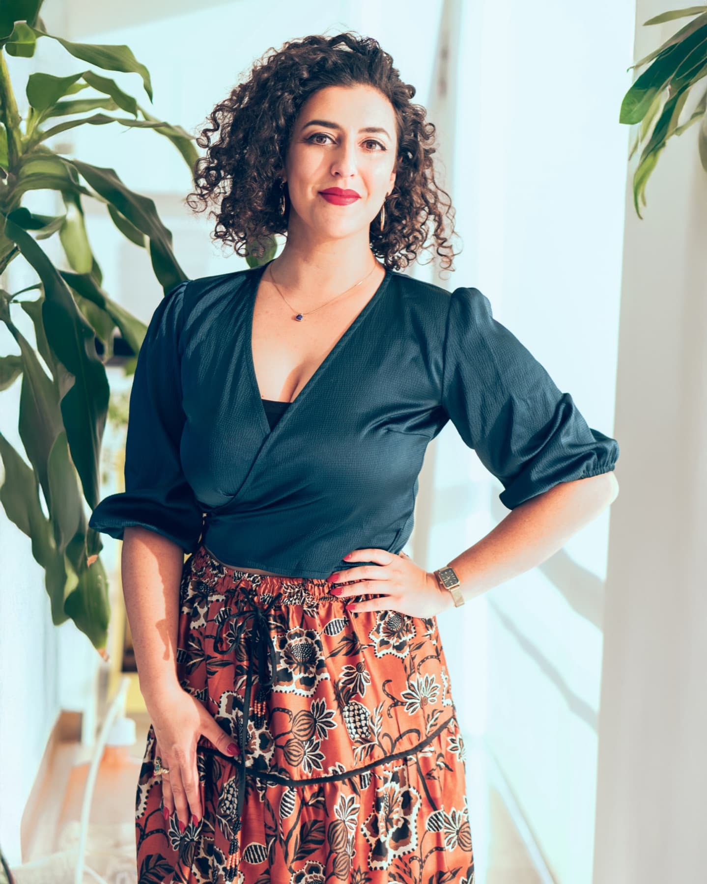 Portrait of Asha Singh, warranted Gestalt psychotherapist, standing beside tall green plants.